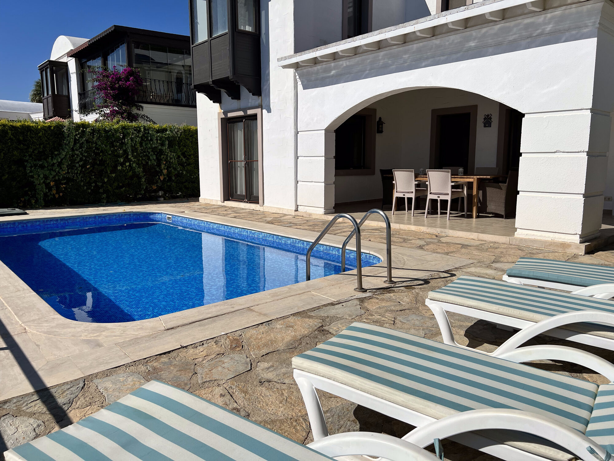 Villa Mia from the garden: white walls, arched covered terrace, private pool and striped sun loungers